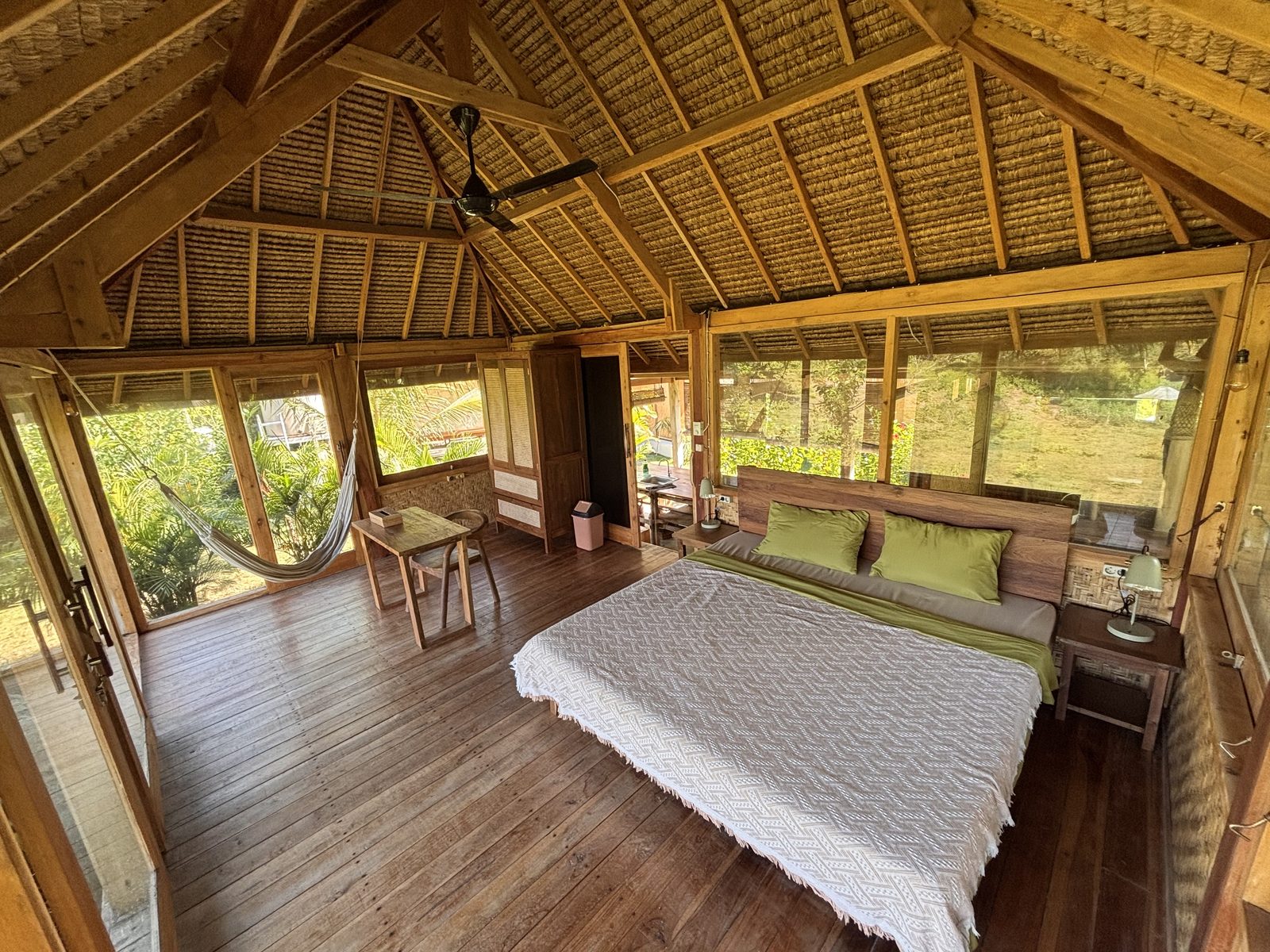 Small Bungalow interior with king bed, antique furniture, hammock, and thatched ceiling